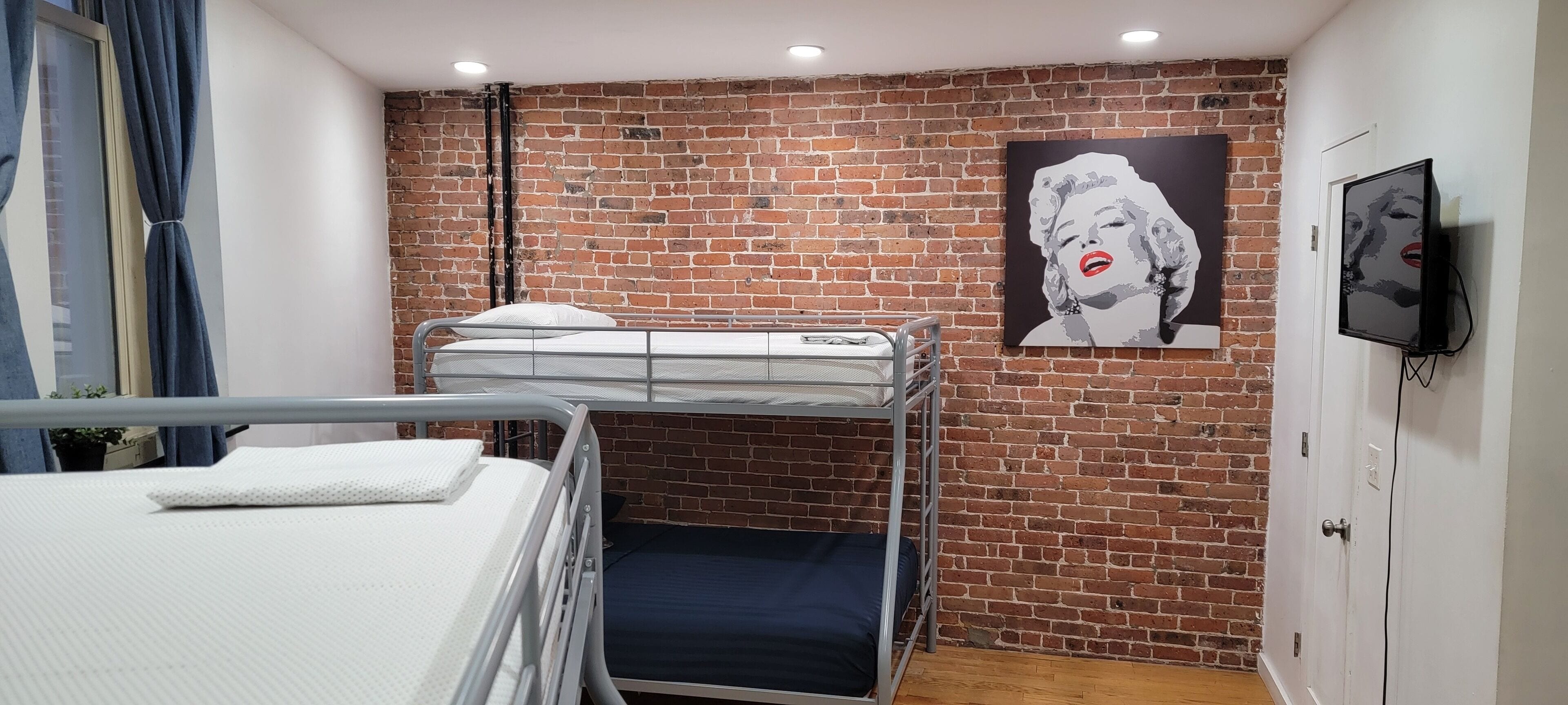 A bunk bed room with a brick wall, a painting, and a TV on the wall.