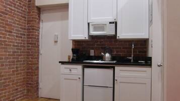 A compact kitchen with white cabinets, a microwave, a kettle, and a coffee maker.