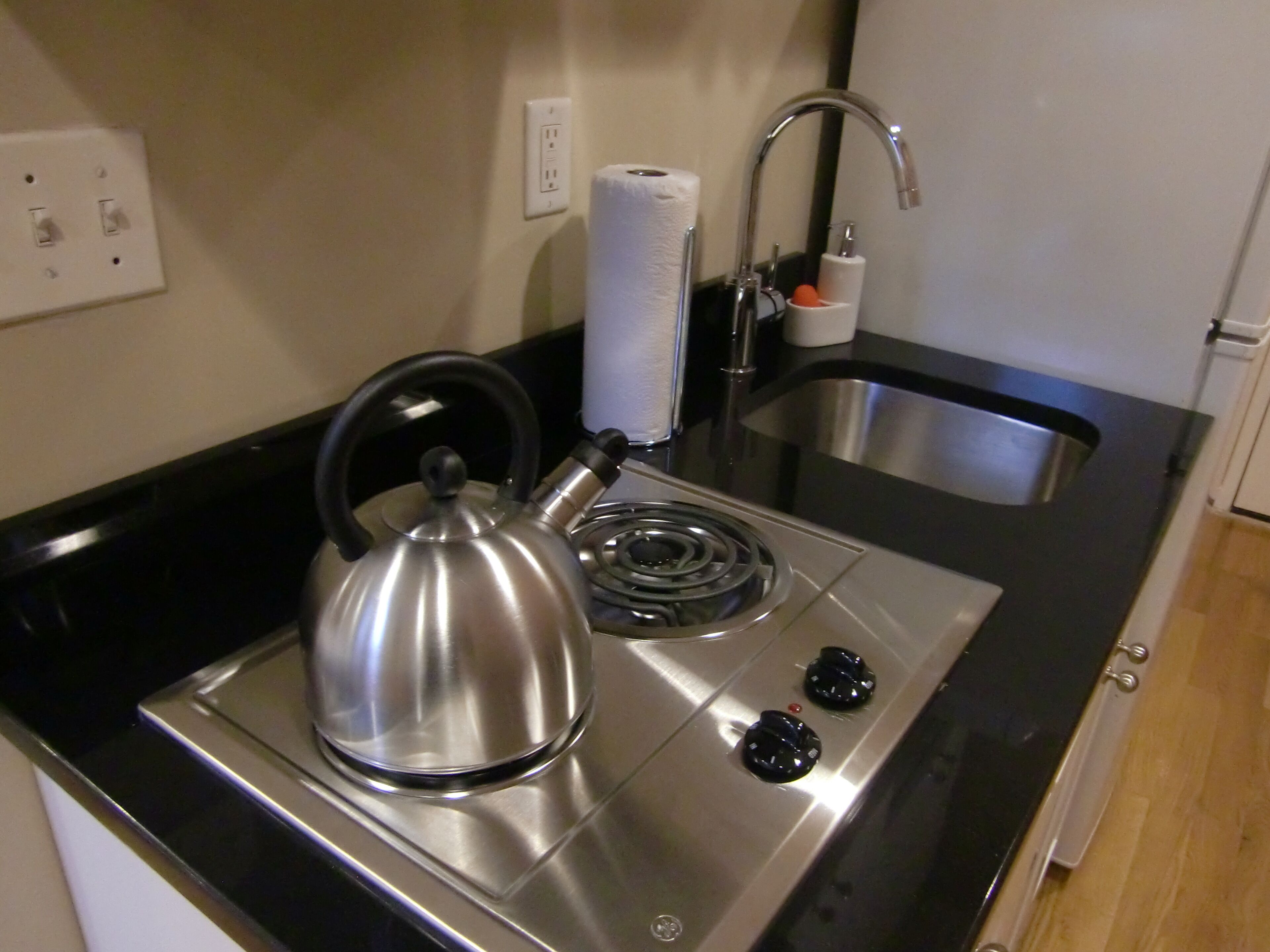 A kitchen with a kettle, a sink, and a stove.