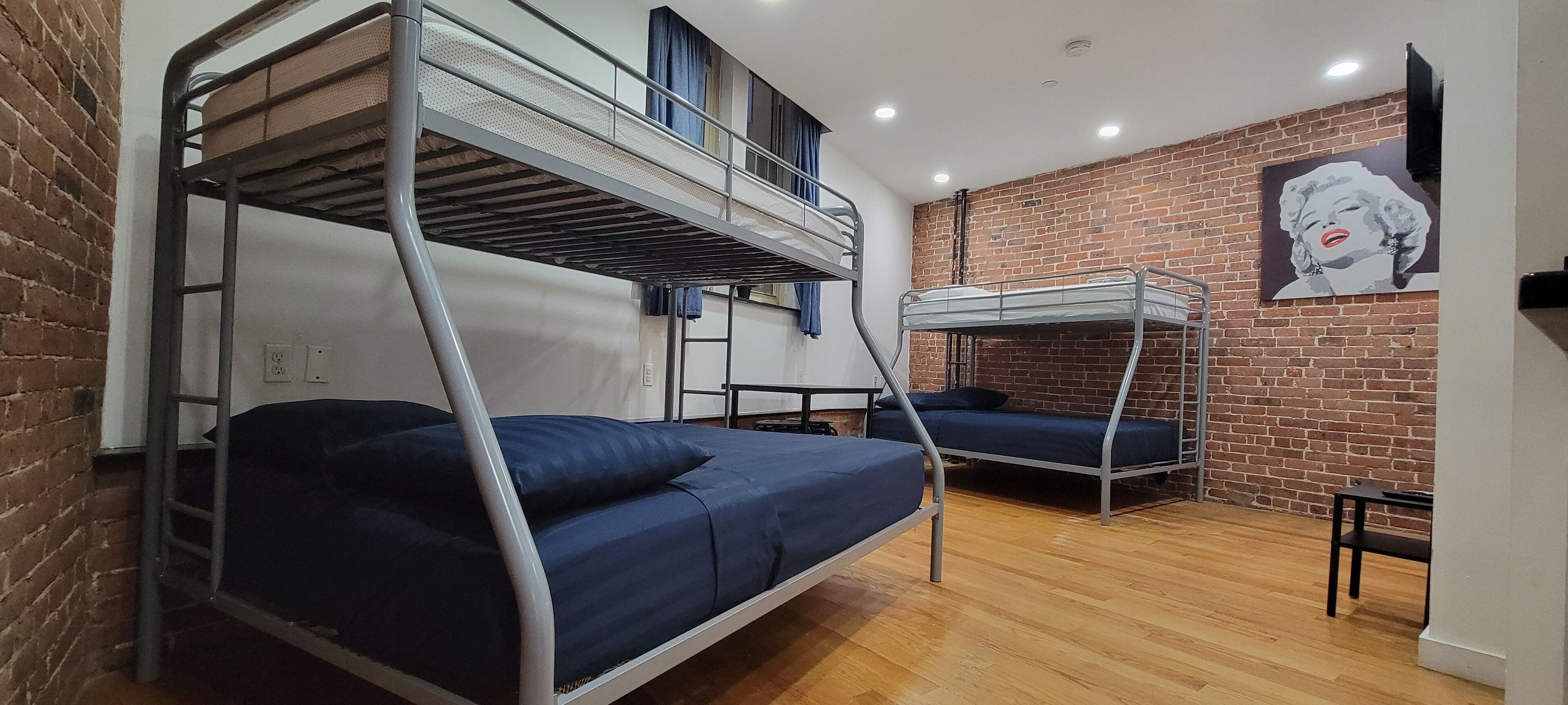 A dormitory room with two bunk beds, a brick wall, a ceiling fan, and a poster on the wall.