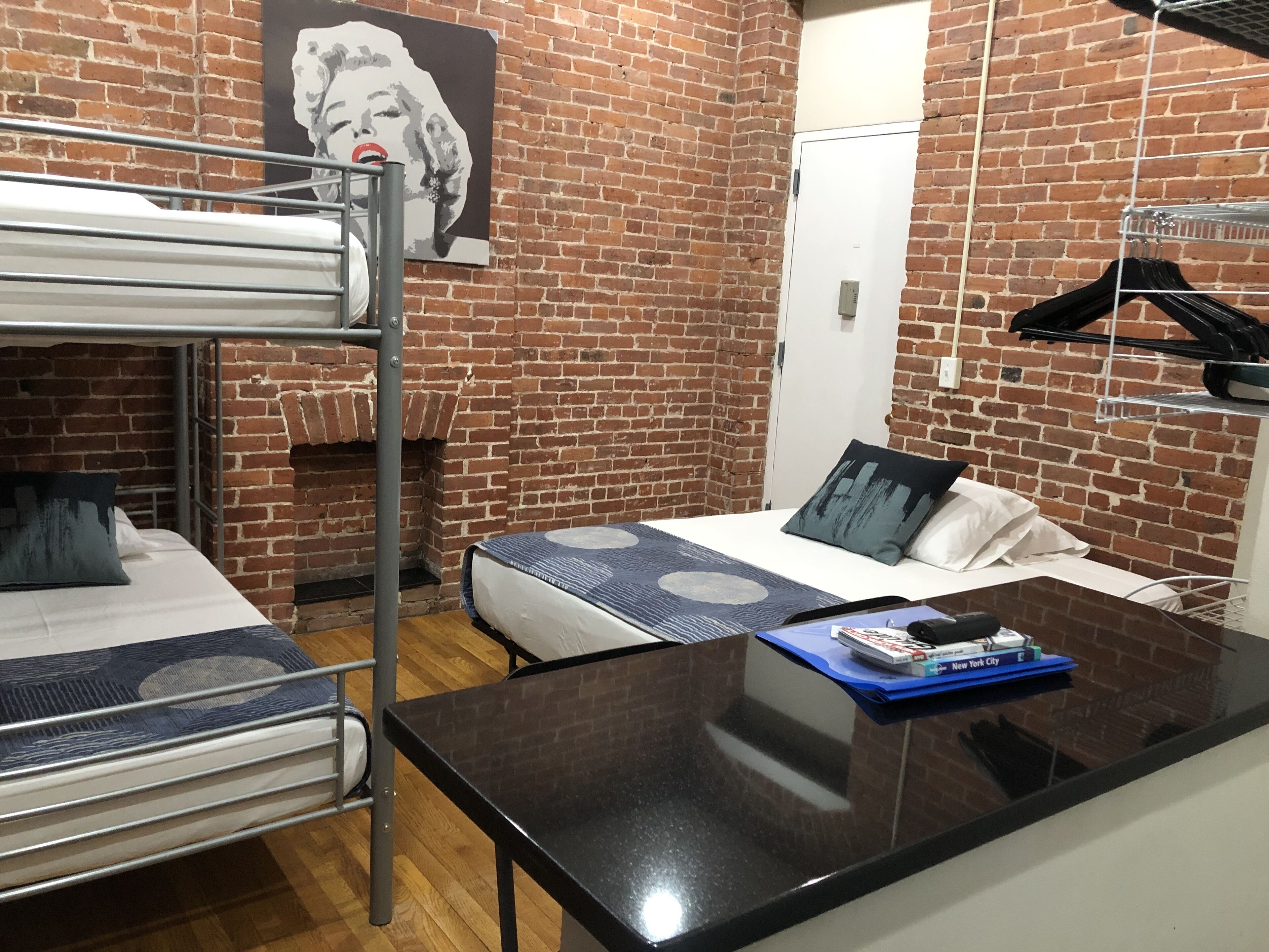 Habitación de residencia estudiantil con una cama individual, una litera y un escritorio. Hay un cuadro en la pared y un perchero.