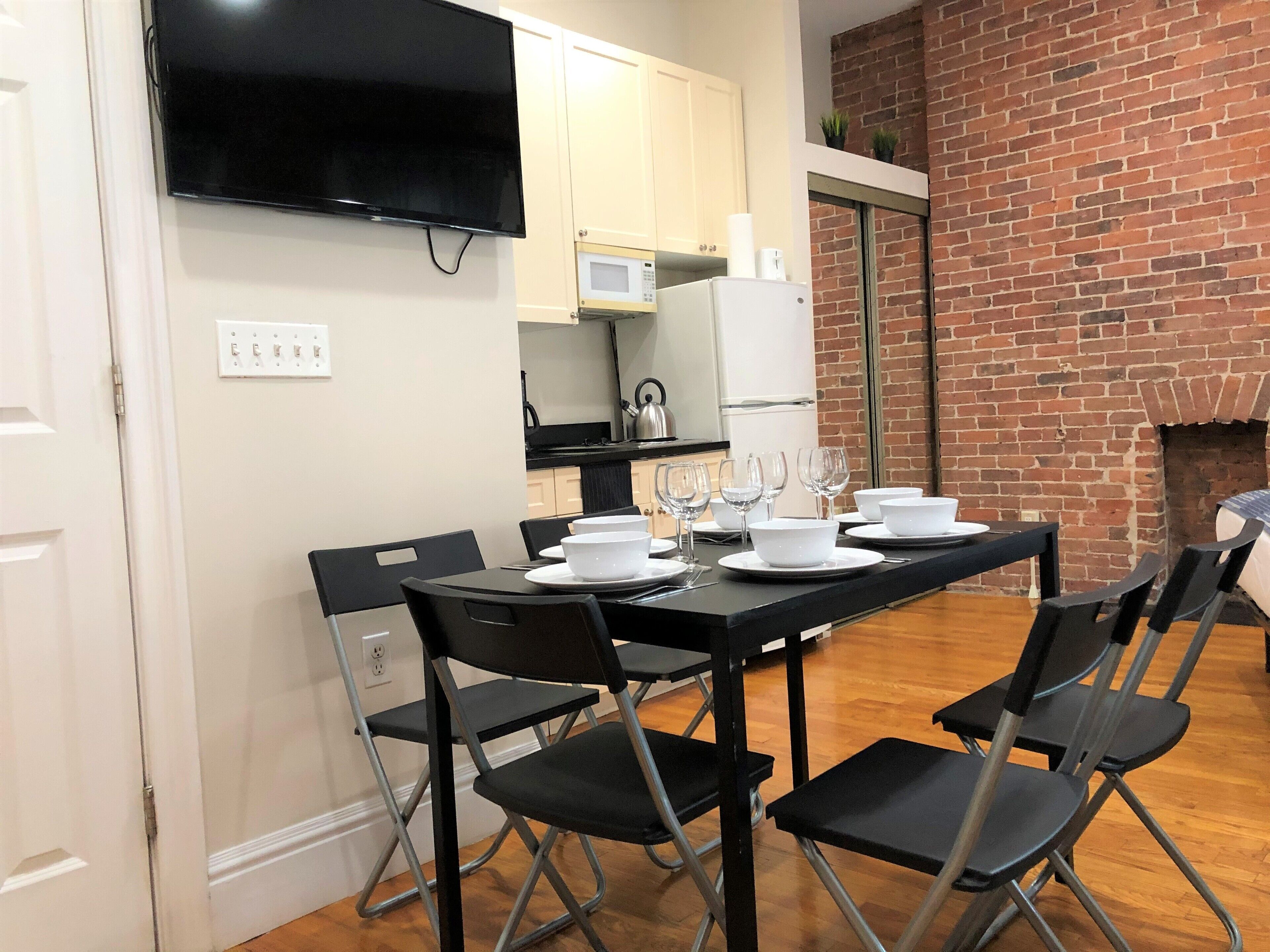 Un coin repas avec une table noire dressée pour six personnes, entourée de chaises noires. Un téléviseur à écran plat est fixé au mur, au-dessus de la table.