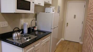 A compact kitchen with white cabinets, a stainless steel kettle, a microwave, a sink, and a refrigerator.