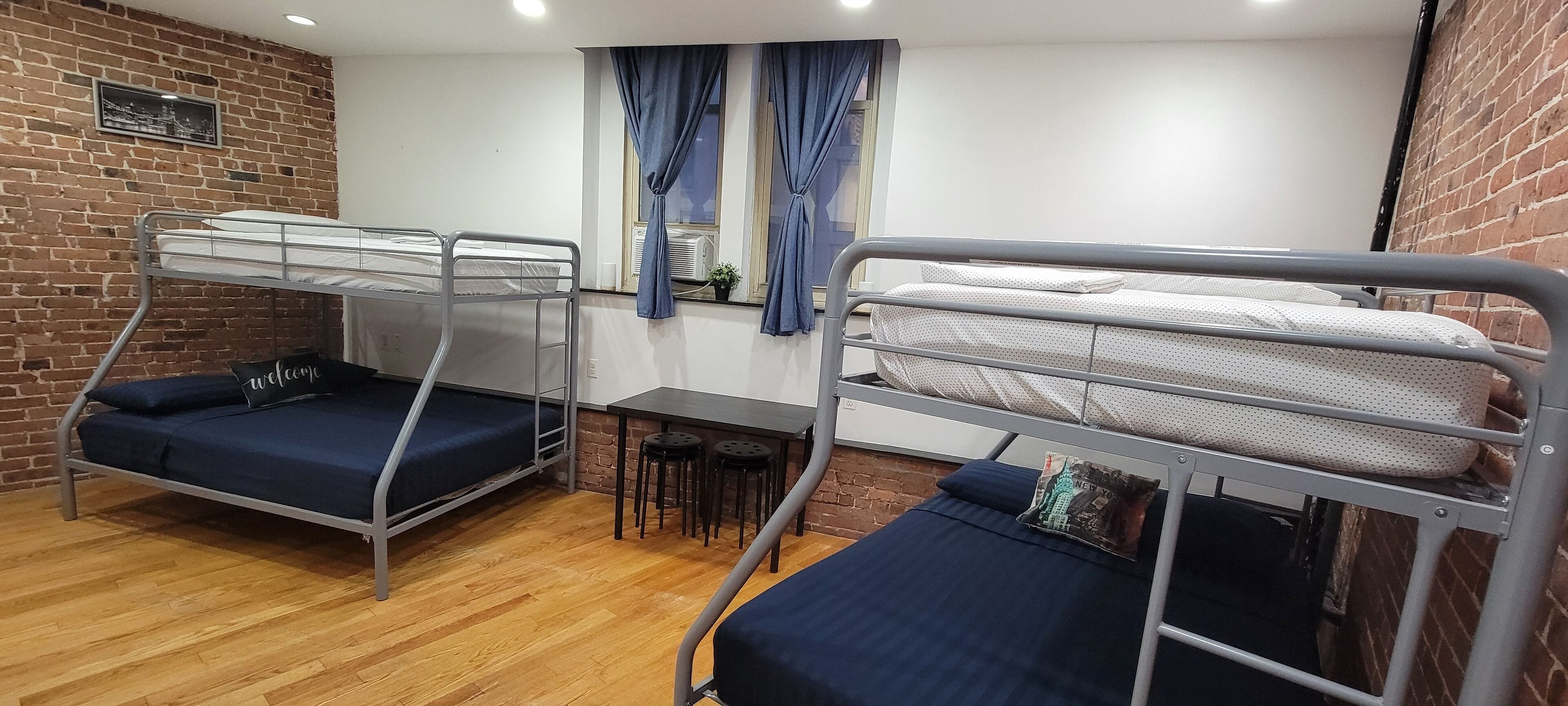 A dormitory room with two bunk beds, a small table, and a window with curtains.