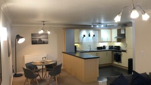 A modern kitchen with a central island, a dining area with a table and chairs, and a living area with a sofa. - River/Meadow View Apartment - Little Paxton (Little Paxton)
