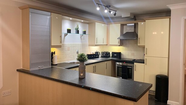 A modern kitchen with a central island, built-in appliances, and a backsplash. - River/Meadow View Apartment - Little Paxton (Little Paxton)