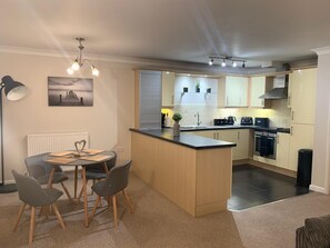 A modern kitchen with a central island, a dining area with a table and chairs, and a view of the kitchen through a window.