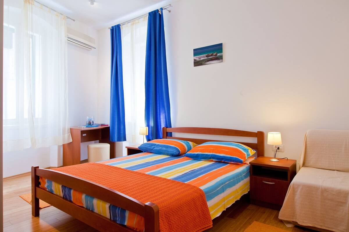 A neatly arranged bedroom with a wooden bed, a bedside table, a nightstand, and a small desk.