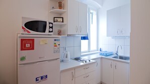 A compact kitchen with white cabinets, a microwave, a kettle, and a sink. - Apartments Val (Split)