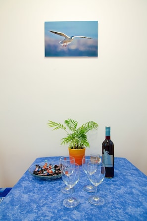A table with a blue tablecloth, a bottle of wine, two wine glasses, a bowl of assorted candies, a potted plant, and a framed picture of a seagull in flight. - Apartments Val (Split)