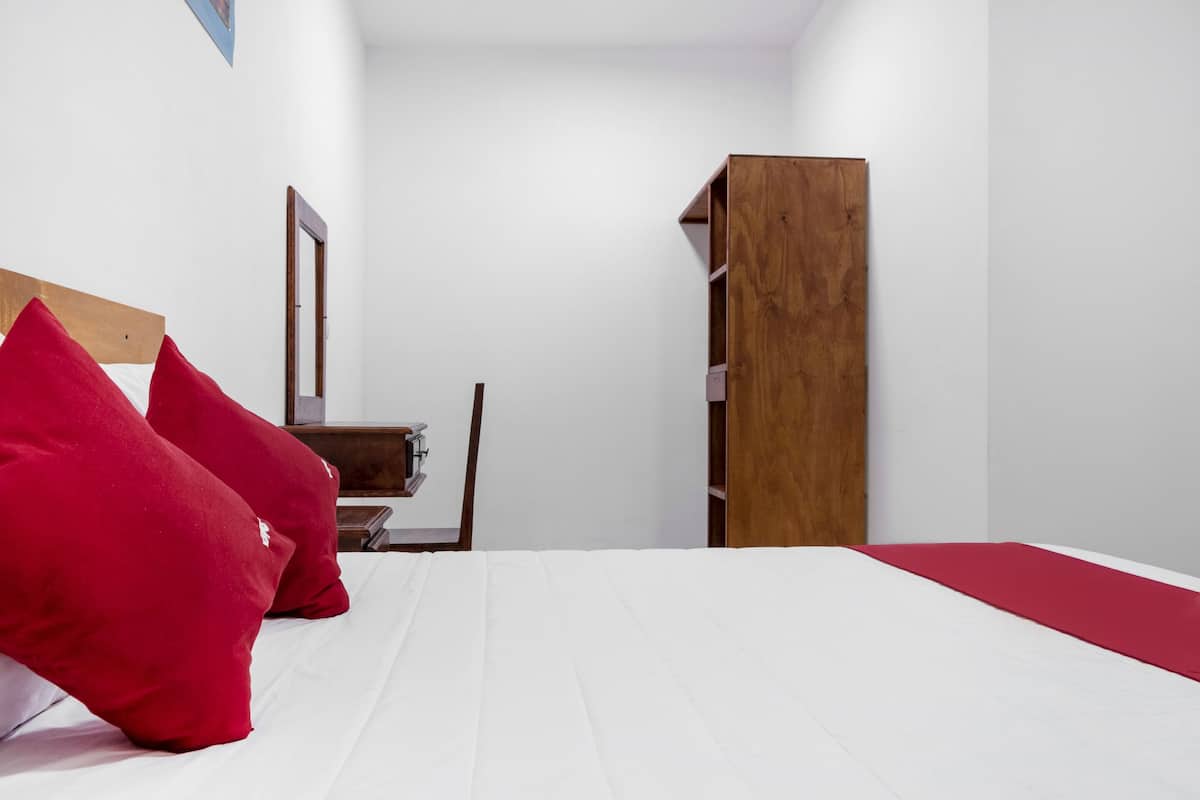 A bedroom with a bed, red pillows, a wooden wardrobe, and a mirror on the wall.
