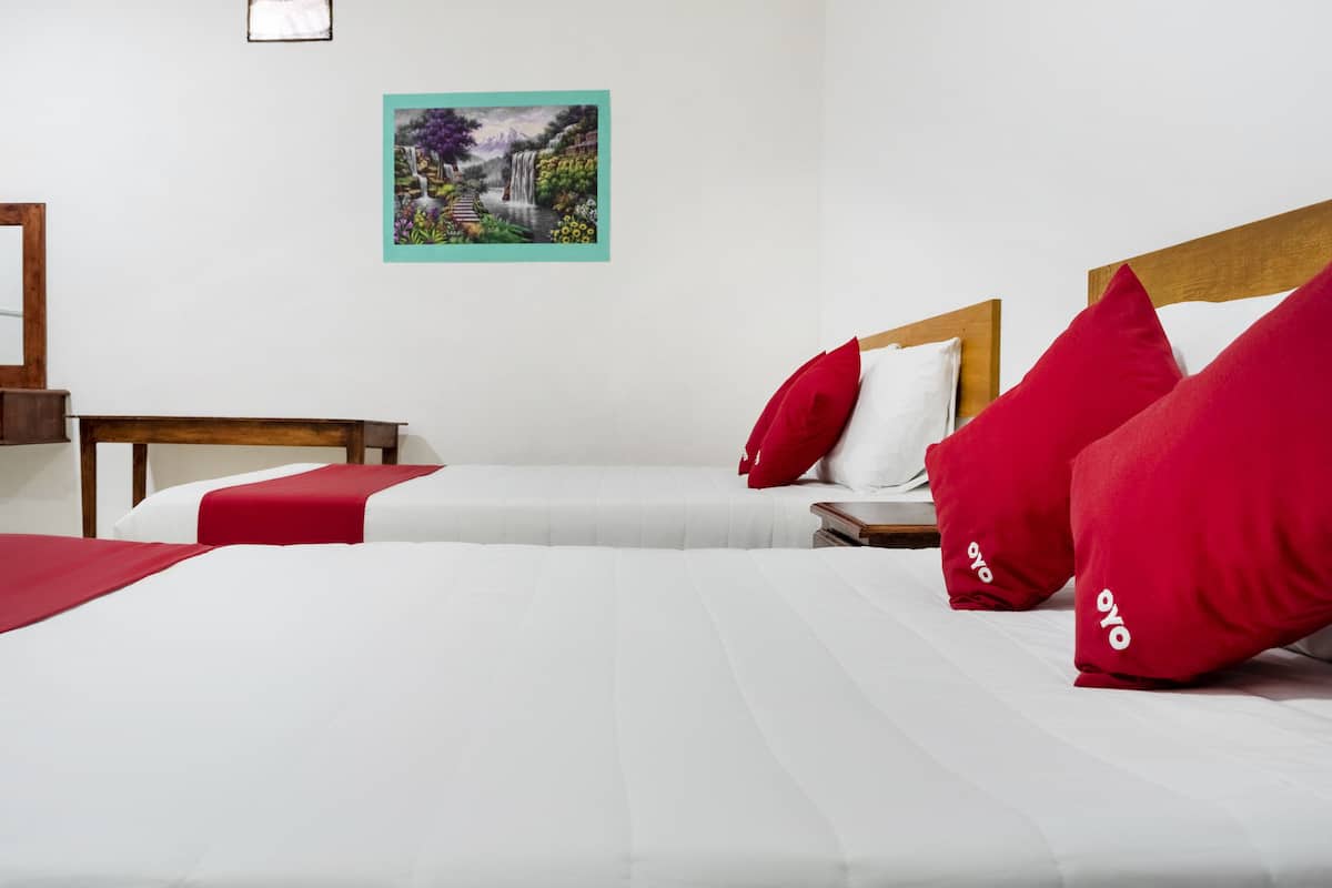 A hotel room with two beds, each with red and white bedding, and a painting of a landscape on the wall.