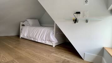 A bedroom with a white bed, wooden flooring, and a sloped ceiling.