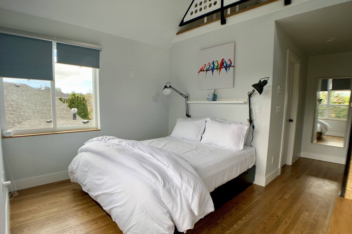 A bedroom with a bed, a window, a painting, and a door.