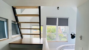 A modern loft bedroom with a wooden staircase, a bed, and a desk area. - Birdhouse on GreenLake (Seattle)