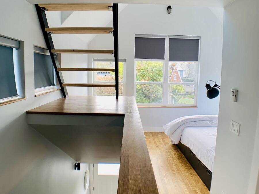 A modern loft bedroom with a wooden staircase, a bed, and a desk area.