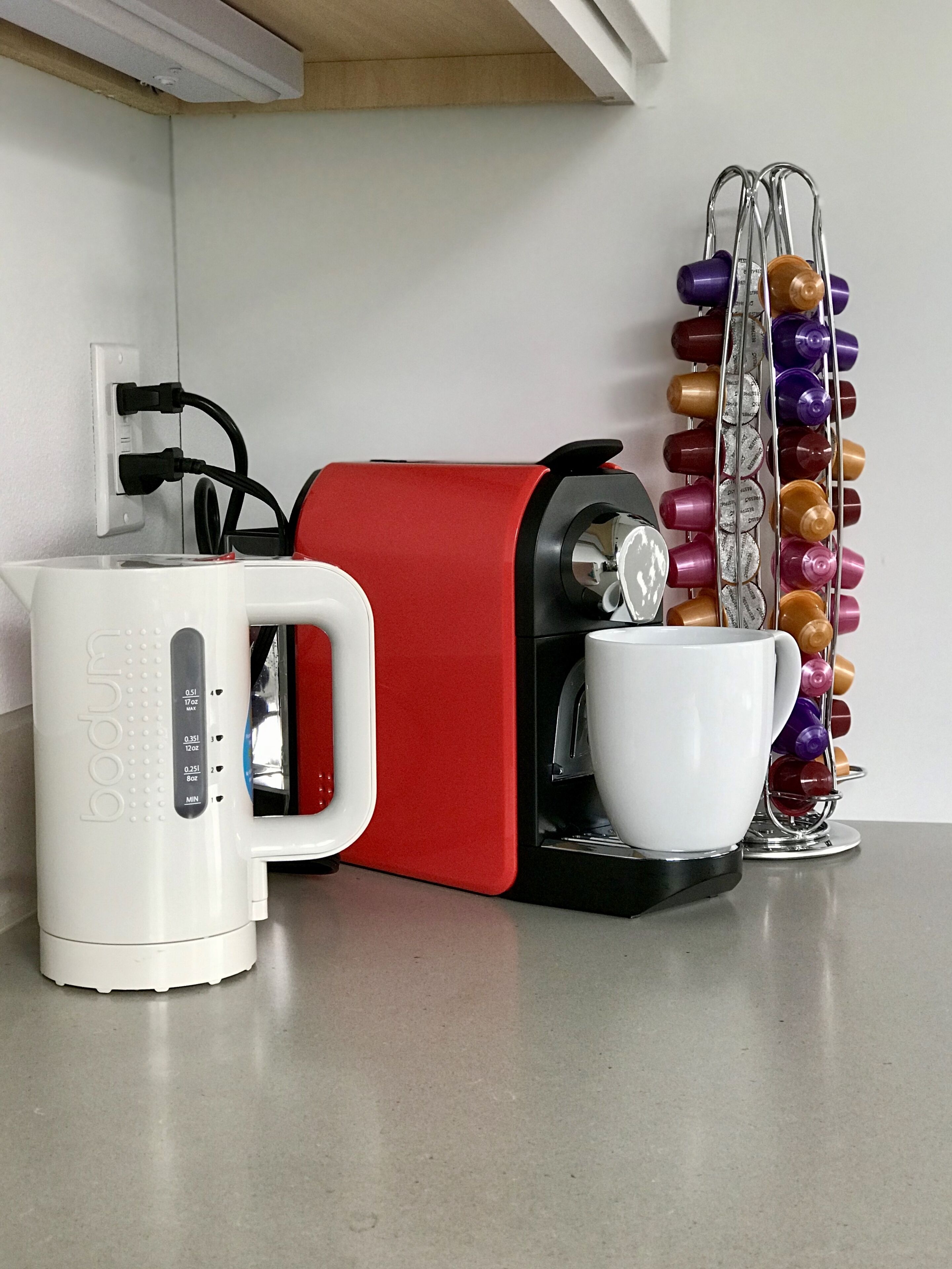 A coffee maker, a white cup, and a bottle holder on a kitchen counter.