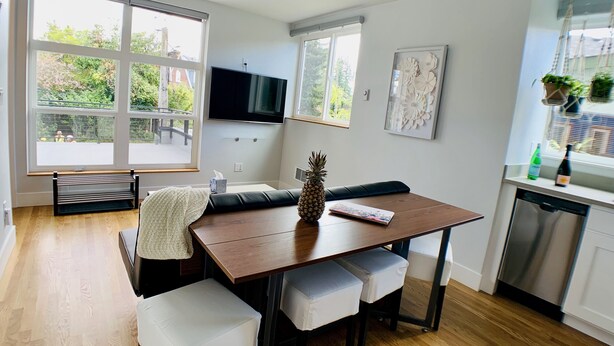 A modern kitchen with a wooden table, white cushioned benches, a pineapple, and a flat-screen TV. - Birdhouse on GreenLake (Seattle)