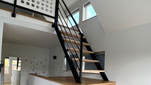 A modern staircase with wooden steps and black railings, leading to an upper level with a white wall and a skylight. - Birdhouse on GreenLake (Seattle)