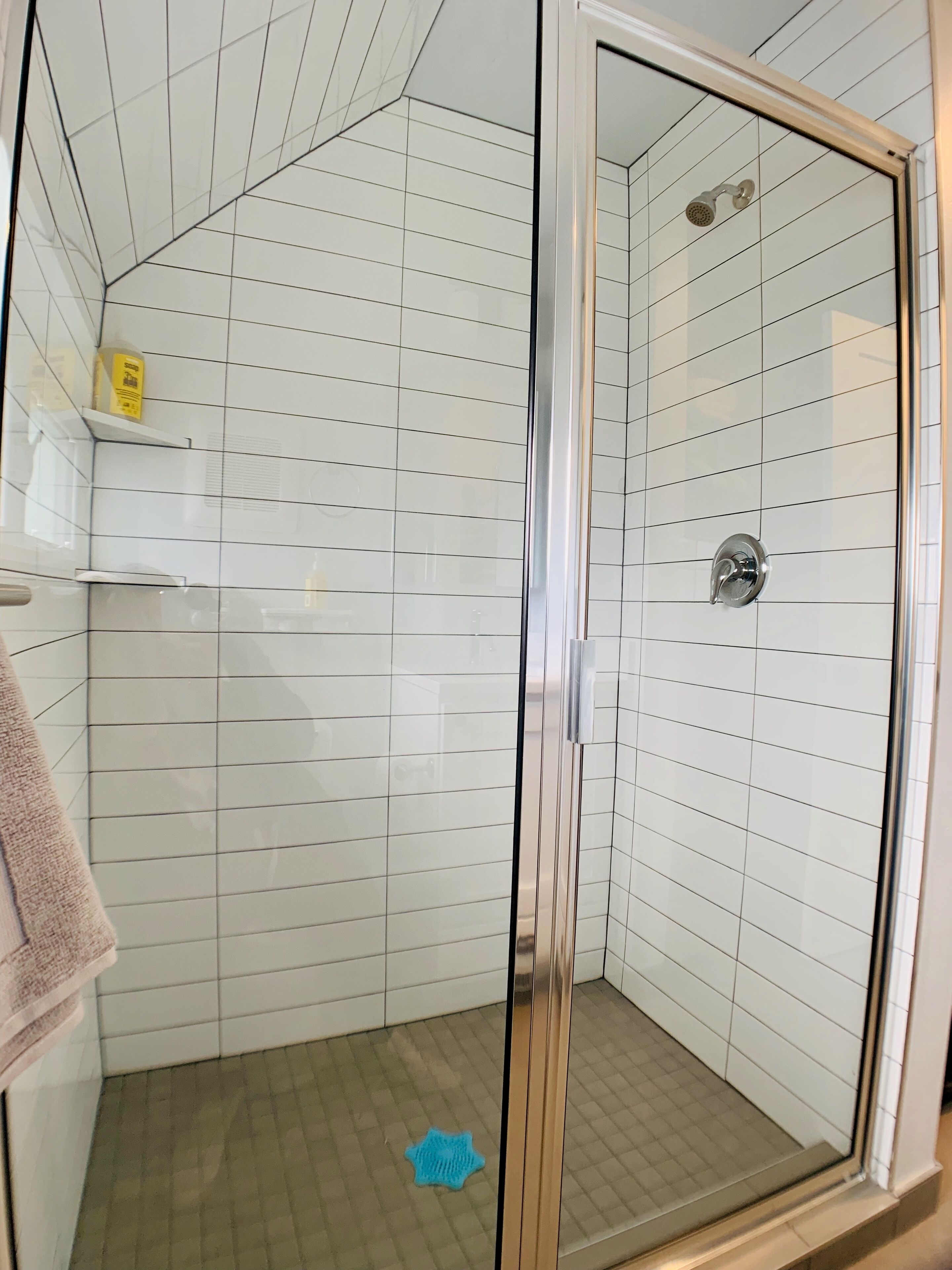 A shower with a glass door, white tiled walls, and a blue mat on the floor.