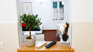 A small indoor plant in a pot, a remote control, and a stack of notebooks on a wooden table.
