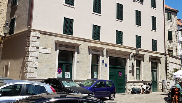 A multi-story building with a flat facade, green shutters, and a ground-level entrance.