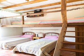 A bunk bed room with wooden beams, two beds with striped bedding, a ladder, and a small shelf with items.