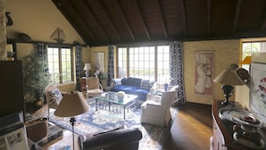 A cozy living room with a blue sofa, striped armchairs, a glass coffee table, and a wooden ceiling. - Historic English Country Lake House  (Lake Oswego)