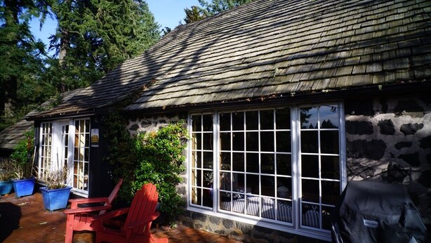 A stone building with a large window, a red chair, and a grill outside. - Historic English Country Lake House  (Lake Oswego)