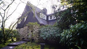 A house with a stone facade, a steeply pitched roof, and a garden with a moss-covered path leading to the entrance. - Historic English Country Lake House  (Lake Oswego)