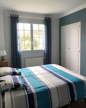 Quarto com cama, janela com cortinas, radiador e porta.
