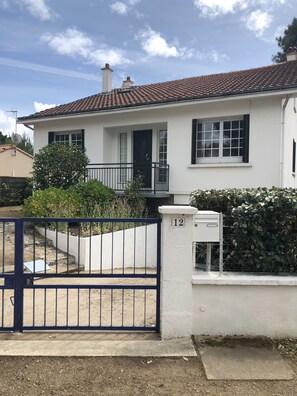 Uma casa branca com telhado de telhas, um portão preto e o número 12 no portão.