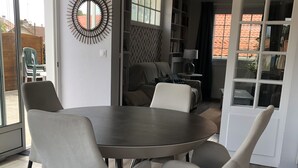 A dining area with a round table and four chairs, a wall-mounted mirror, and a view of the outside through a sliding door.
