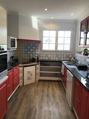 Cozinha compacta com armários vermelhos, micro-ondas, pia e janela que proporciona iluminação natural.