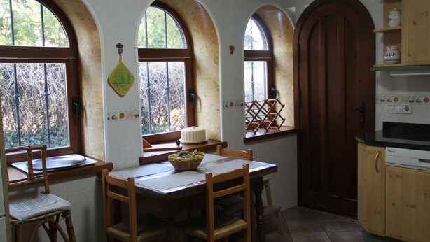 A kitchen with a wooden table, chairs, and a window with a view of trees. - Chalet House Honorato San Rafael routes of (San Rafael)