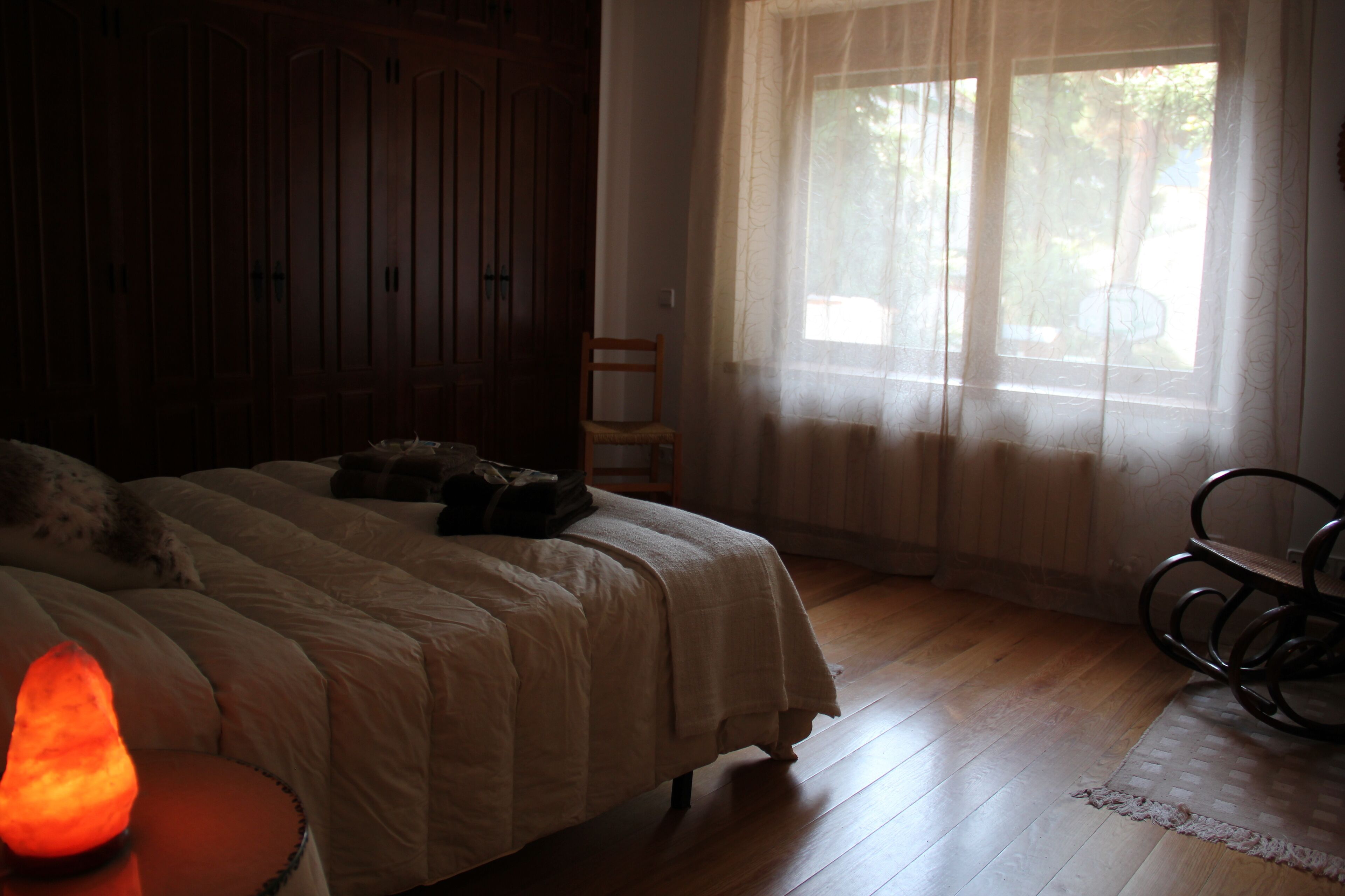 A bedroom with a bed, a chair, a heater, and a window with curtains.