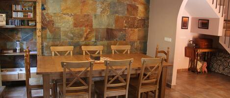 A dining area with a wooden table and chairs, a stone wall, and a staircase.