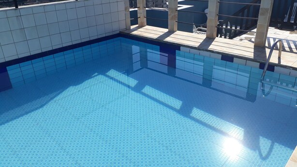 A clear blue pool with tiled edges and a tiled deck area. - Apartamentos 54M e 62C (Guarujá)