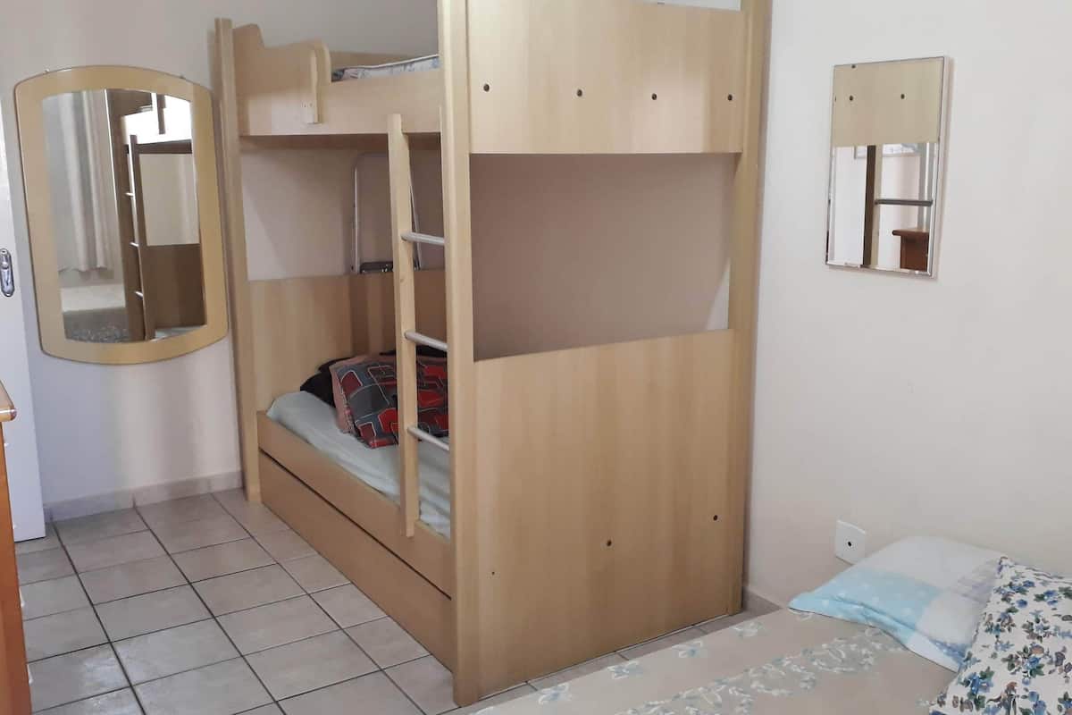 Ein Stockbett mit einer Stehleiter, ein kleiner Nachttisch, ein Spiegel und ein Einzelbett mit blumigem Überwurf.
