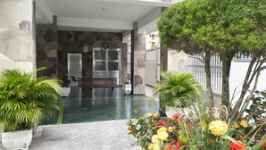 A covered entrance with a bench, potted plants, and a tiled floor. - Apartamentos 54M e 62C (Guarujá)