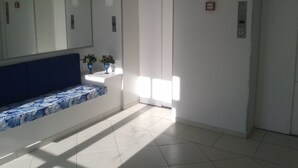 A hallway with a bench, a door, and a wall-mounted mirror. - Apartamentos 54M e 62C (Guarujá)