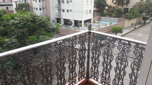 A balcony with ornate metal railings overlooking a residential area with buildings, a swimming pool, and greenery. - Apartamentos 54M e 62C (Guarujá)