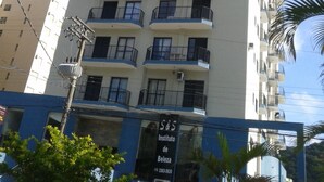 A tall, multi-story building with balconies and a sign for 'Instituto de Belza' at the bottom. - Apartamentos 54M e 62C (Guarujá)