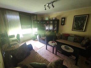A living room with a sofa, armchair, and a coffee table. There is a bookshelf, a clock, and a framed picture on the wall.