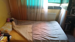 Ein Einzelbett mit einer Decke, ein Nachttisch mit einem Buch und ein Fenster mit Vorhängen.