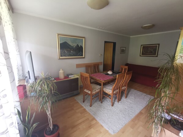 A dining area with a wooden table and chairs, a painting on the wall, and potted plants.