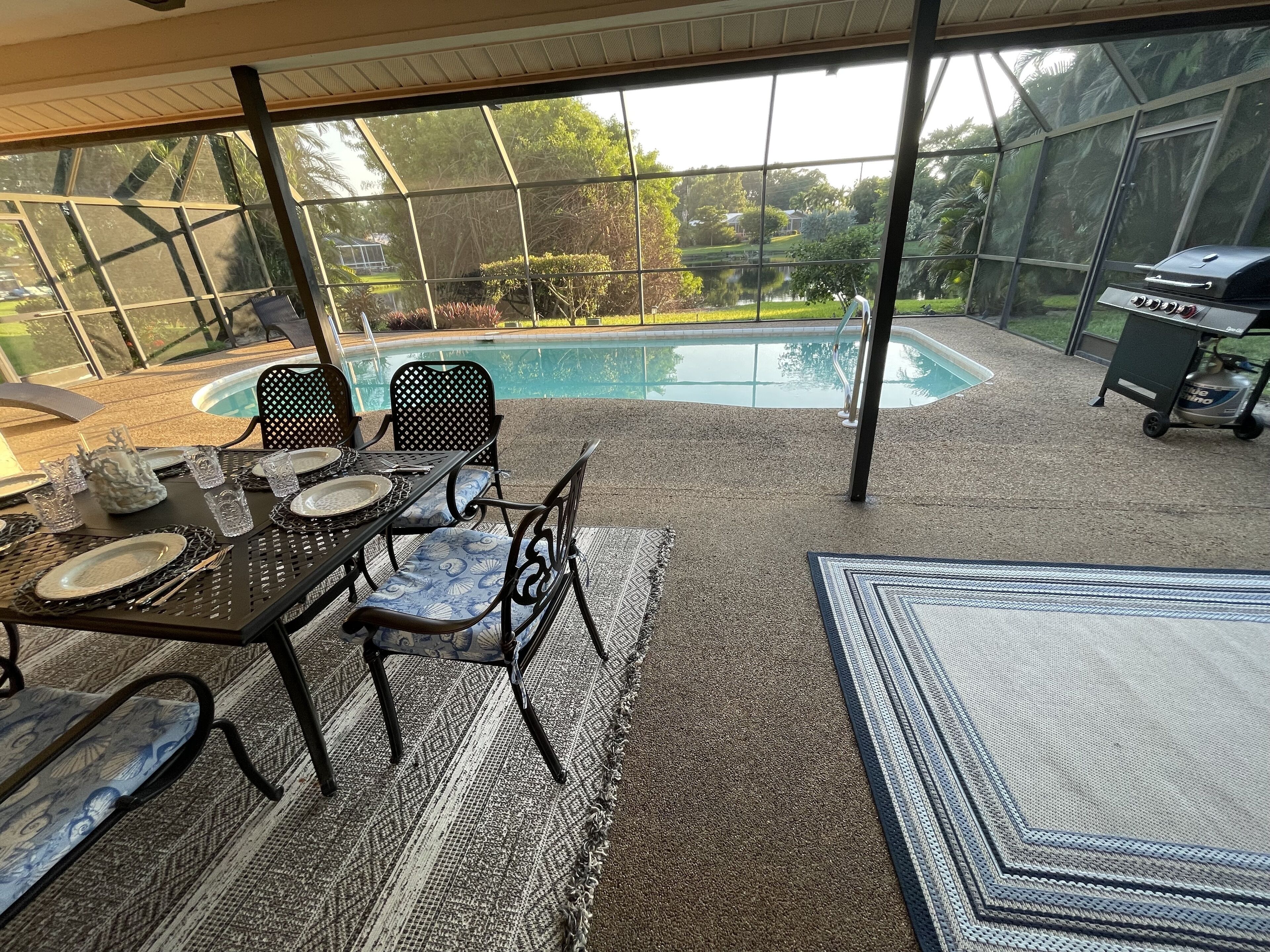 An outdoor patio area with a table set for dining, surrounded by chairs, and a view of a swimming pool.