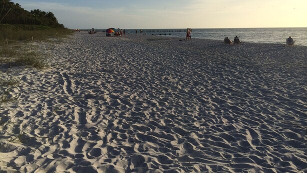 Een zandstrand met enkele mensen en een felgekleurde parasol.