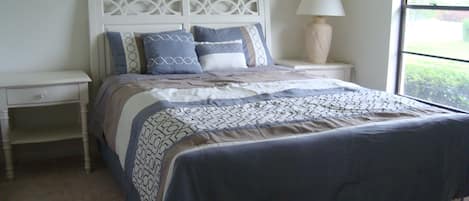 Un lit bien fait, recouvert d’une couvre-lit à motifs, avec une lampe de chevet et une table de nuit.