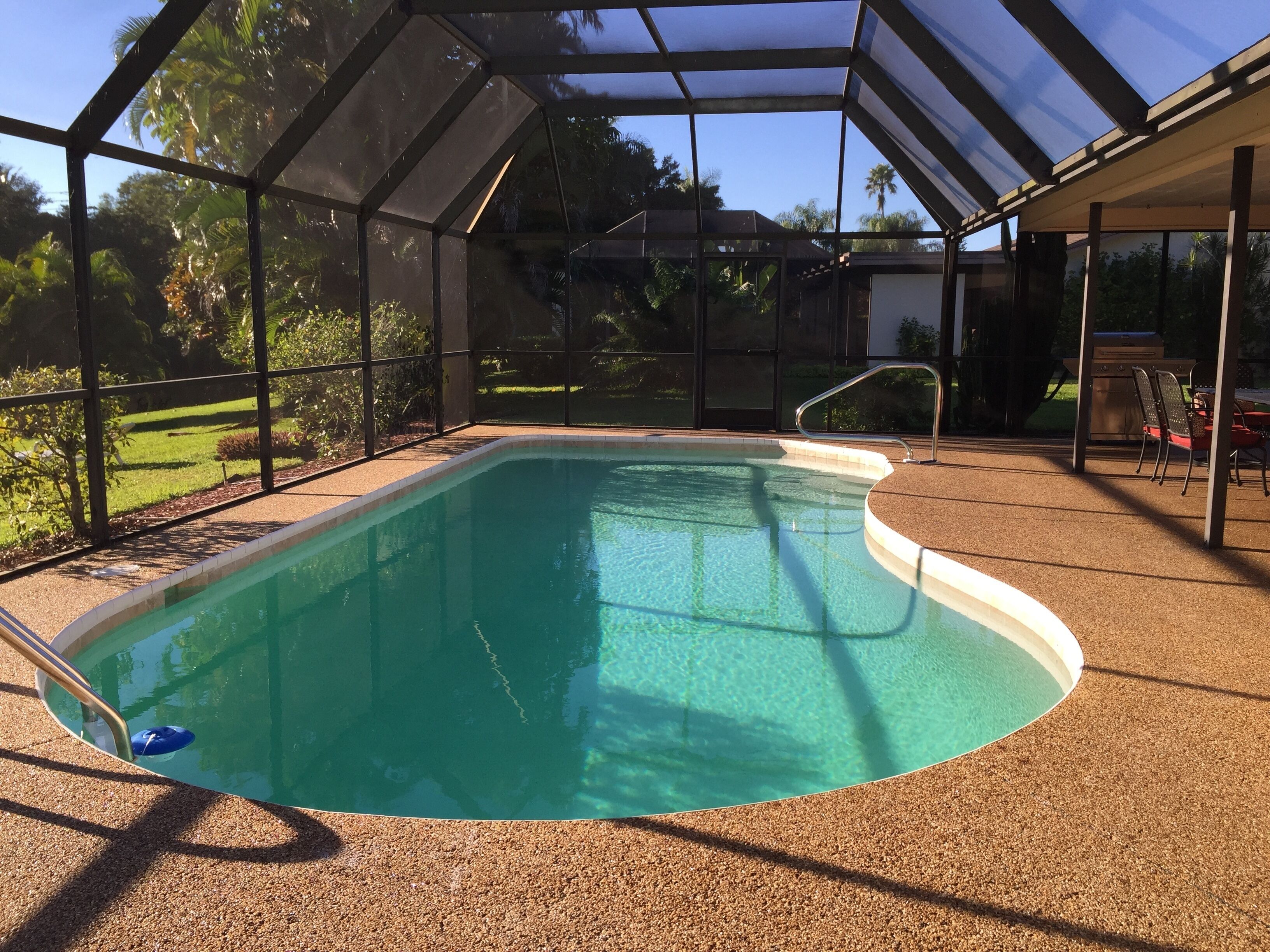 Une piscine dotée d’une enceinte en verre, entourée d’une terrasse en gravier et d’un patio couvert.